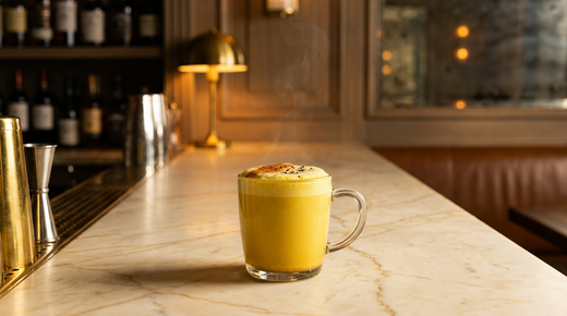 Golden milk jaune doré dans un mug de verre, mousse légère, cannelle et poivre concassé, comptoir de marbre crème