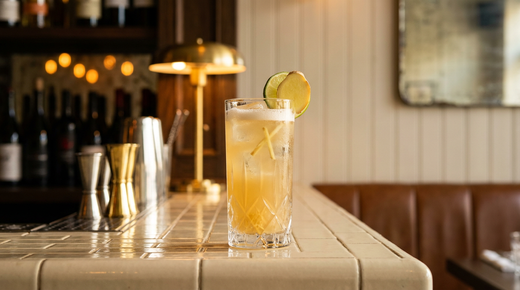 Ginger beer maison dorée et trouble dans un grand verre, mousse fine et rondelle de gingembre, comptoir de brique émaillée