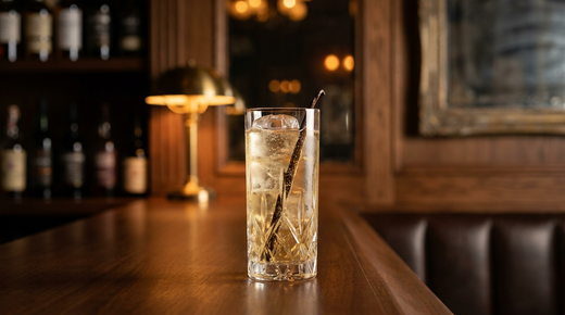 Vanille tonic très pâle dans un grand verre sur glace, gousse de vanille fendue dressée dedans, comptoir de caviste