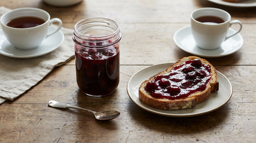 Pot de confiture de cerises, tartine de pain de campagne, tasse de thé noir