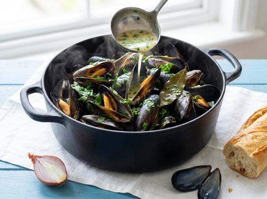 Sauce marière au vin blanc et persil ladlée sur des moules ouvertes dans une cocotte en fonte, échalote et baguette