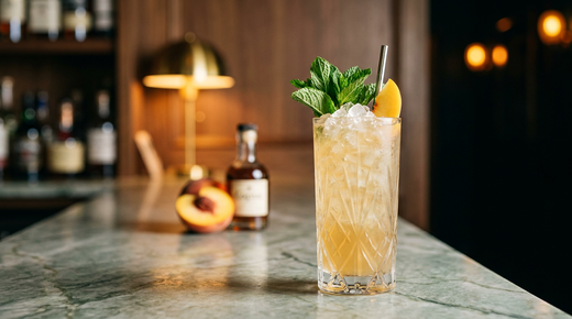 Georgia Mint Julep doré pâle sur glace pilée dans un grand verre taillé, bouquet de menthe et quartier de pêche, comptoir de quartzite Sea Pearl