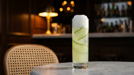 Gin fizz au concombre dans un verre haut, col de mousse blanche, rubans de concombre à l'intérieur, table de terrasse en marbre