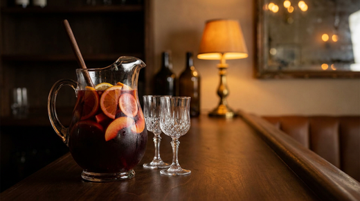 Grand pichet en verre de sangria sans alcool rouge sombre avec rondelles d'orange, de citron et quartiers de pêche, comptoir de bois ciré sombre