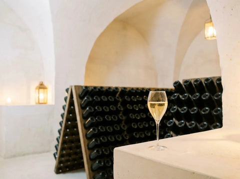 Crayère champenoise aux murs de craie blanche éclairée à la lampe, pupitres de remuage et verre de champagne doré posé sur un rebord de craie.