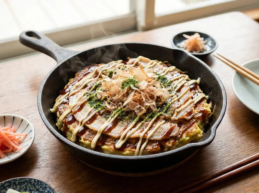 Okonomiyaki d’Osaka : galette japonaise épaisse au chou garnie de porc, nappée de sauce brune en zigzag, de mayonnaise, de bonite séchée et d’algue verte