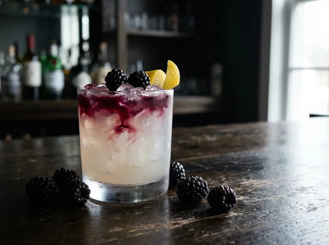 Bramble violet sur glace pilée en verre bas, liqueur de mûre coulée sur le dessus, mûres et citron en garniture
