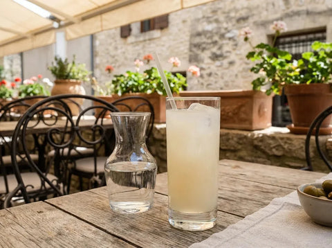 Mauresque laiteuse dans un grand verre avec glace et carafe d'eau, sur une terrasse de café provençal ensoleillée