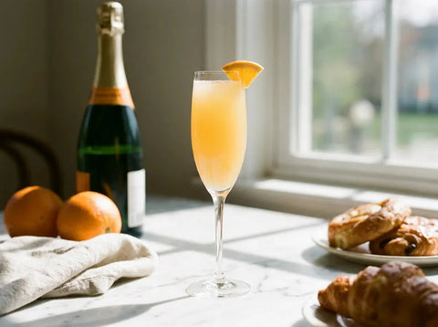 Mimosa orange pâle à fines bulles en flûte, tranche d'orange, bouteille de bulles et oranges sur table de brunch