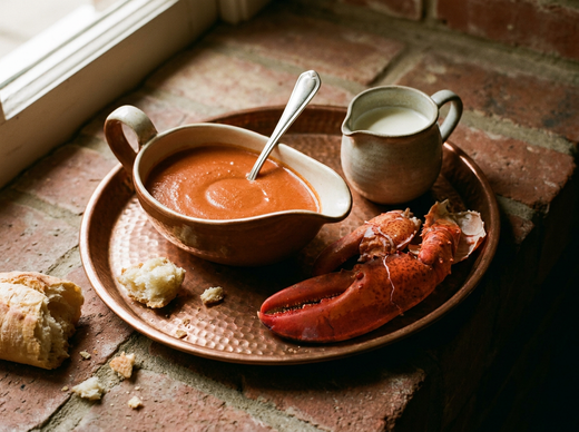 Sauce cardinal rouge corail au homard dans une saucière en grès, pince de homard et pot de crème sur un plateau en cuivre