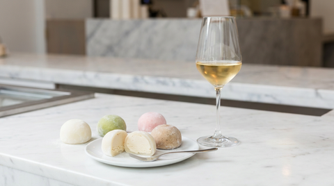 Mochis glacés pastel sur marbre, un mochi coupé montrant la glace, verre de vin doux