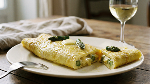Omelette roulée baveuse aux asperges vertes en gros plan, beurre fondu, assiette ivoire, verre de vin blanc