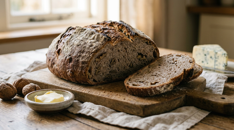 Pain aux noix ouvert sur une planche, mie gris-brun truffée de cerneaux, tranche épaisse, beurre et noix en coque