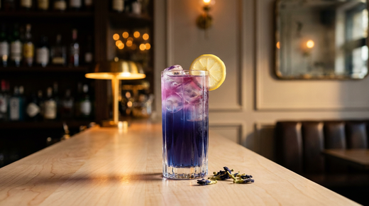 Limonade au butterfly pea bleu indigo virant au violet rose en haut du verre, rondelle de citron et fleurs séchées, comptoir de sycomore