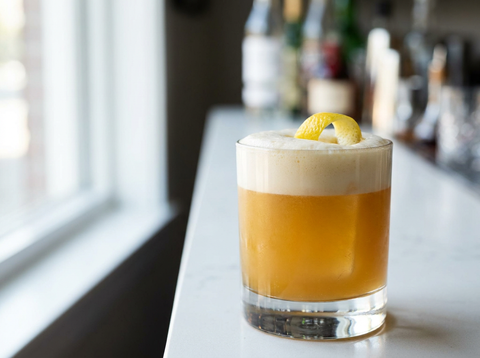 Armagnac Sour dans un verre bas, mousse de blanc d'œuf soyeuse sur robe dorée ambrée