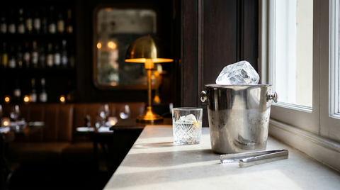 Seau à glace en argent contenant un bloc de glace translucide, pince et verre bas