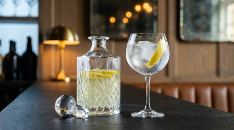 Carafe de gin pré-dosé aux zestes de citron et verre ballon de gin tonic sur un comptoir d'ardoise