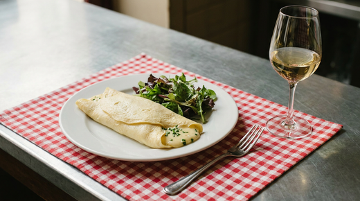 Omelette au fromage roulée et baveuse, comté fondu, salade verte, nappe à carreaux, verre de vin blanc