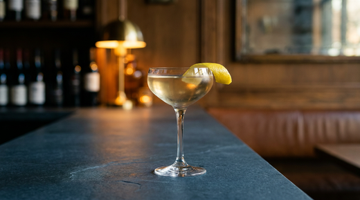 London Calling ambre pâle et limpide dans une coupe, long zeste de citron sur le bord, comptoir d'ardoise bleu gris