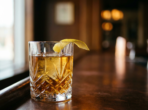 Rusty Nail servi sur un gros glaçon dans un verre old fashioned, robe ambrée dorée et zeste de citron