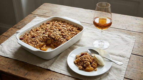 Crumble aux pommes doré dans son plat, part servie avec crème fraîche, verre de vin doux