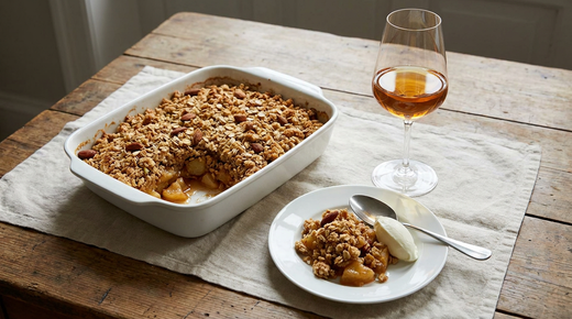 Crumble aux pommes doré dans son plat, part servie avec crème fraîche, verre de vin doux