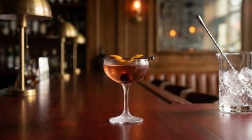 Gin and It ambre rosé limpide dans une coupe glacée, cerise et zeste d'orange, comptoir d'acajou ciré