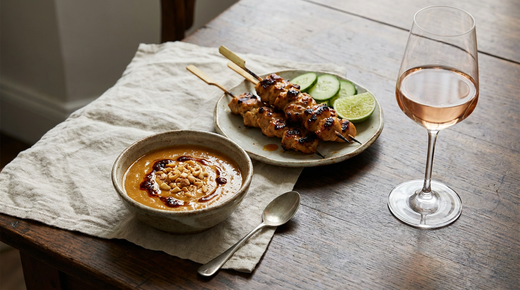 Bol de sauce satay aux cacahuètes, brochettes de poulet grillées, verre de rosé
