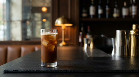Café glacé en cocktail dans un grand verre sur glace, fine couche de crème en surface, plaque d'ardoise noire