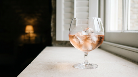 Rosé piscine dans un verre ballon sur gros glaçons, appui de fenêtre en pierre