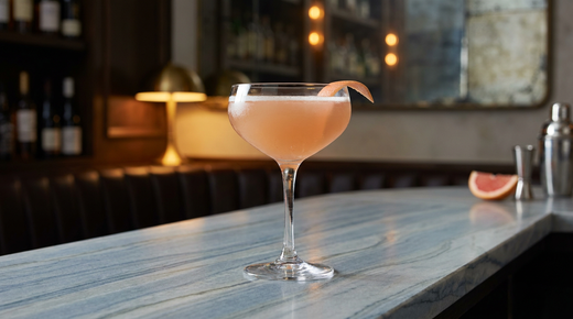 Palm Beach rosé ambré légèrement voilé dans une coupe glacée, ruban de zeste de pamplemousse rose, comptoir de quartzite Azul Macaubas