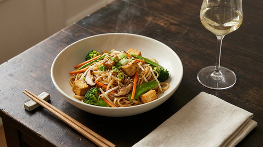Bol de nouilles sautées au tofu doré et légumes croquants, verre de vin blanc