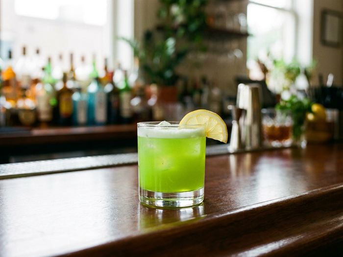 Midori Sour : cocktail vert vif à la liqueur de melon sur glace, tranche de citron, comptoir de bar