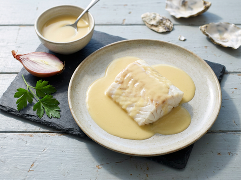Sauce au vin blanc dorée nappant un pavé de poisson poché, échalote coupée et coquilles d’huîtres sur une ardoise