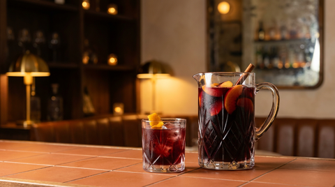 Zurracapote dans un pichet en verre avec pêches et bâton de cannelle, un verre servi devant, comptoir en tomettes