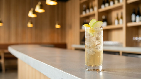 Cocktail gin et jus de pomme en grand verre sur le comptoir de béton d'un bar à vins, lamelles de pomme verte