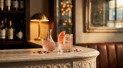 Sirop de rose rose vif dans une bouteille de verre, pétales frais à côté, table de bois flotté gris