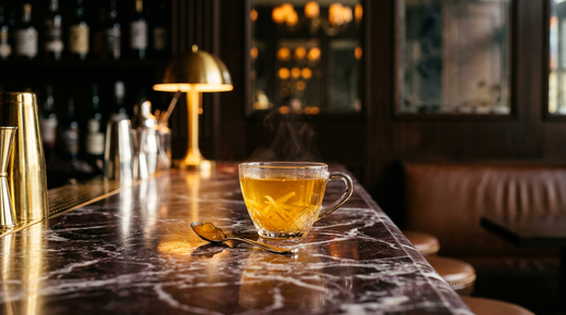 Yuja-cha doré fumant dans une tasse en verre avec des lanières d'écorce confite en suspension, comptoir de marbre Rosso Levanto