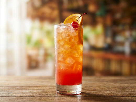 Rum punch planteur jamaïcain dans un verre highball avec glace pilée, dégradé rouge orangé, tranche d'orange