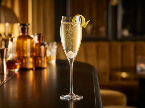 Champagne cocktail dans une flûte : vin pétillant doré, sucre au fond, zeste de citron, bar tamisé