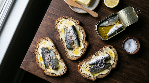 Tartines de pain de campagne au beurre demi-sel épais et sardines entières à l'huile, rondelles d'échalote et poivre concassé, boîte de sardines ouverte encore pleine d'huile dorée, demi-citron et bol de gros sel