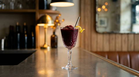 Frozen vin rouge en granité rouge foncé dans un verre à pied, zeste de citron, plan de bar en inox