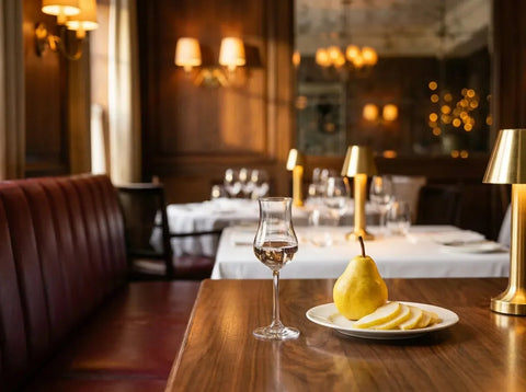Petit verre tulipe d'eau-de-vie de poire williams limpide et incolore, à côté d'une poire jaune entière et de quelques tranches, dans un bistrot chic