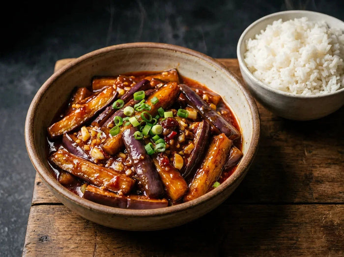 Aubergines sichuanaises yuxiang au wok : bâtonnets d’aubergine fondants dans une sauce brune brillante à l’ail, gingembre et piment, parsemés d’oignon vert