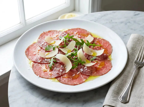 Carpaccio de bœuf : fines tranches de bœuf cru sur une assiette, copeaux de parmesan, roquette, huile d’olive et citron