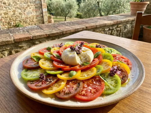Carpaccio de tomates multicolores en rosace avec une burrata crémeuse ouverte au centre, basilic frais et filet d’huile d’olive