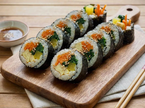 Rondelles de kimbap coréen sur une planche : riz à l’algue nori garni de carotte, épinards, omelette et radis jaune, sections colorées