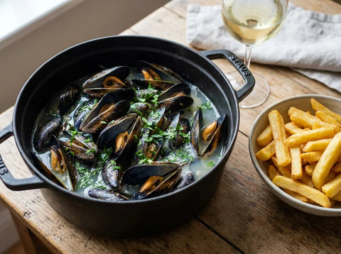 Moules marinières dans une cocotte noire avec bouillon au vin blanc, persil et frites