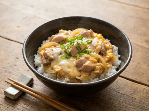 Bol d’oyakodon japonais : morceaux de poulet et oignon liés à l’œuf coulant sur un riz blanc, parsemé d’oignon nouveau