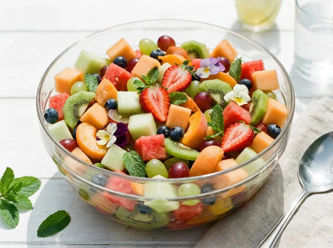 Salade de fruits d’été colorée dans un saladier : melon, pêche, abricot, fraises, kiwi et raisin, feuilles de menthe fraîche